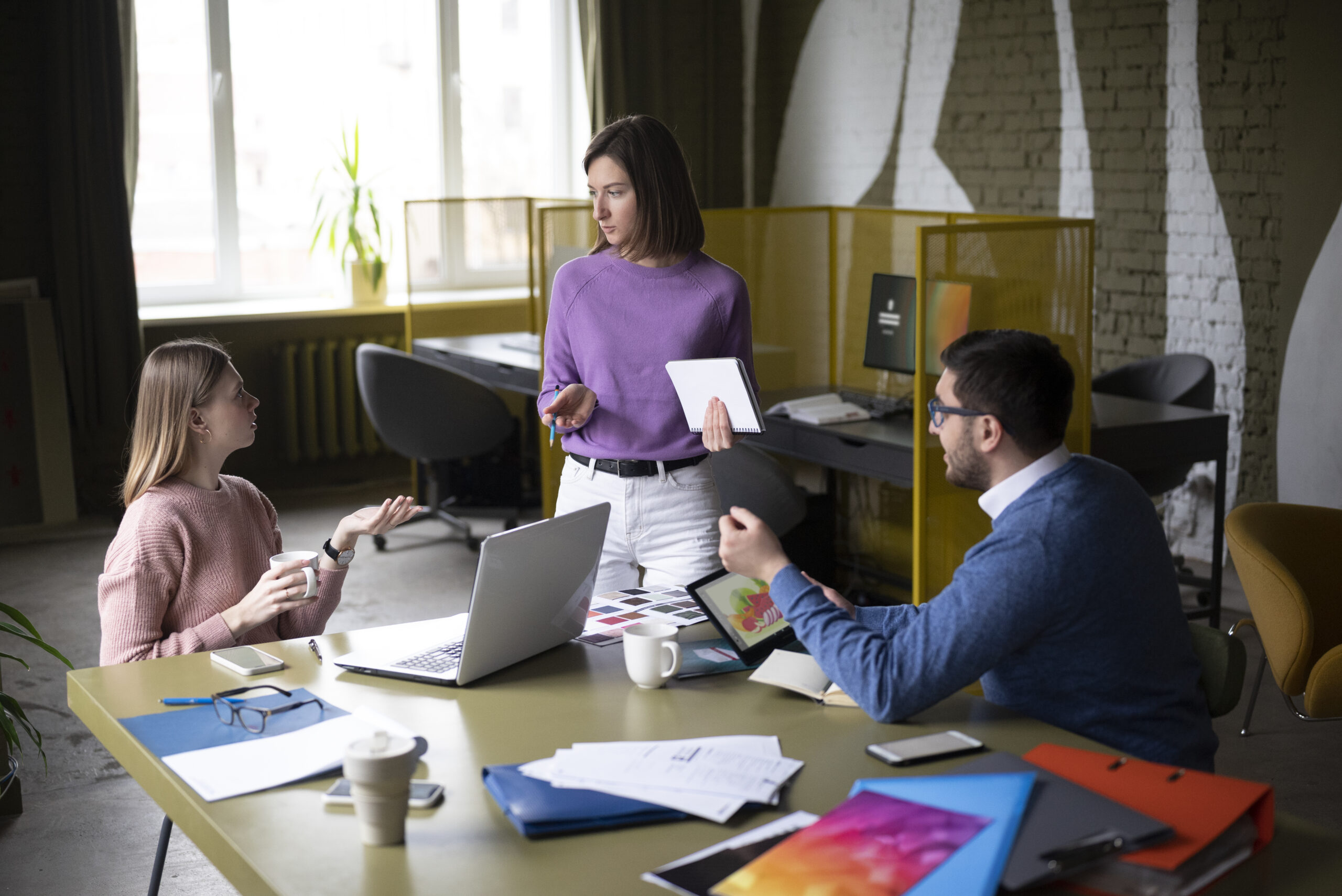 A group of young professionals with laptops, tablets, and papers on the table in a contemporary workplace are generating ideas.